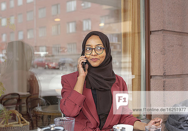Lächelnde Frau in einem Café  die über ihr Handy spricht