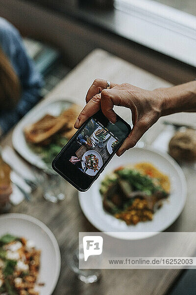 Hand mit Handy fotografiert Essen auf dem Tisch