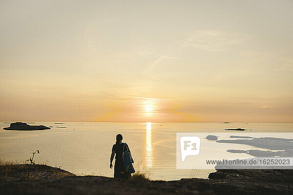 Frau an felsiger Küste bei Sonnenuntergang