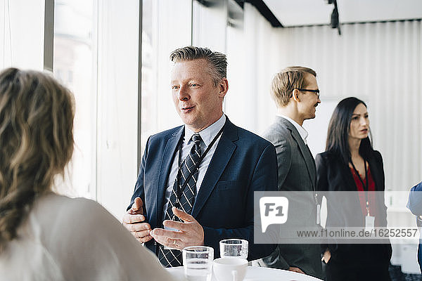 Male entrepreneur talking to colleague while coworker standing in background at workplace