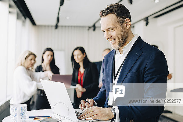 Lächelnder Geschäftsmann arbeitet über Laptop  während er im Büro steht Seminar