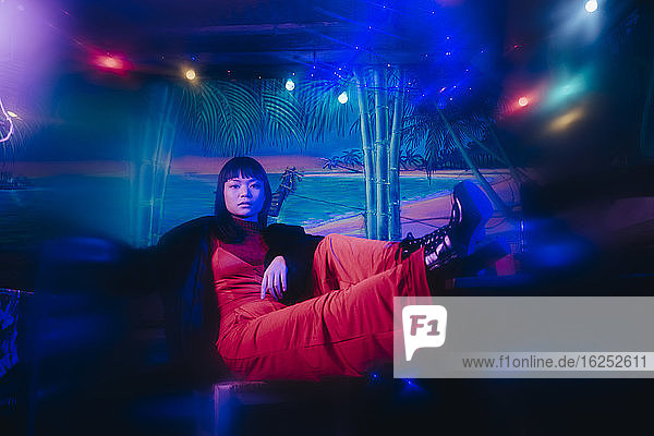 Ganzflächiges Porträt einer jungen  modischen Frau  die an einer beleuchteten Restaurantbar sitzt