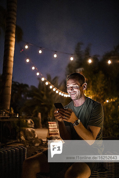 Smiling man texting while sitting outdoors during sunset