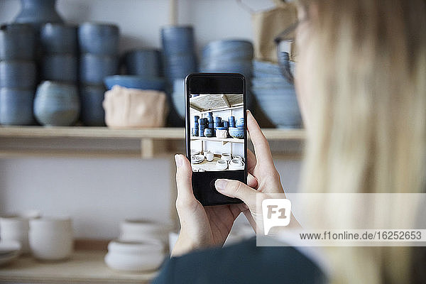 Cropped image of woman photographing earthenware with smart phone in art studio