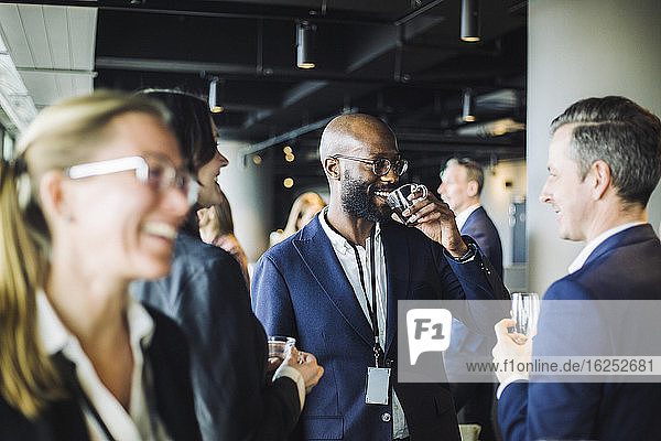Lächelnder Unternehmer trinkt schwarzen Kaffee  während er mit Kollegen im Büro steht