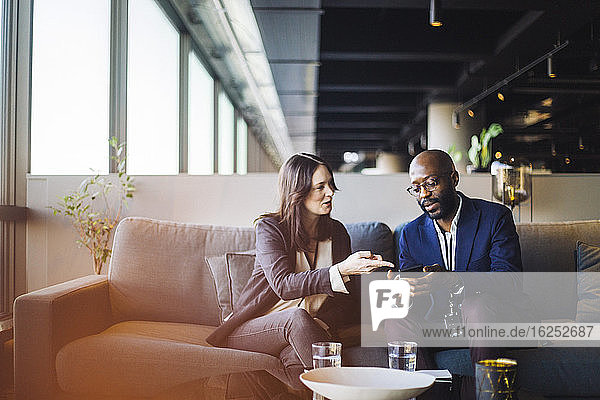 Geschäftsmann zeigt Geschäftsfrau ein Smartphone  während er im Büro sitzt