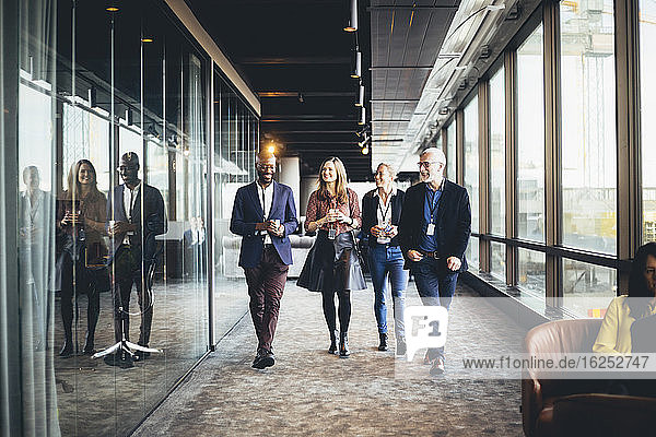 Lächelnde weibliche und männliche Kollegen gehen am Arbeitsplatz im Korridor
