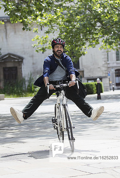 Playful businessman riding bicycle on sunny city sidewalk
