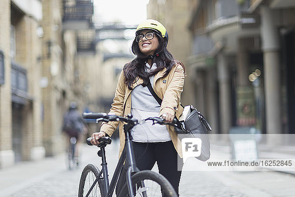 Portrait smiling woman in helmet with bicycle on city street