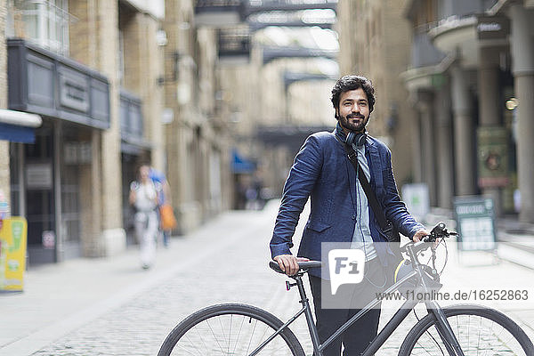 Portrait confident businessman with bicycle in city street