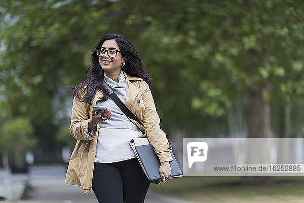 Lächelnde Geschäftsfrau geht mit Smartphone im Park