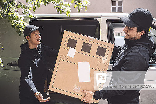 Lächelnde Zusteller halten Pappkarton neben Lastwagen