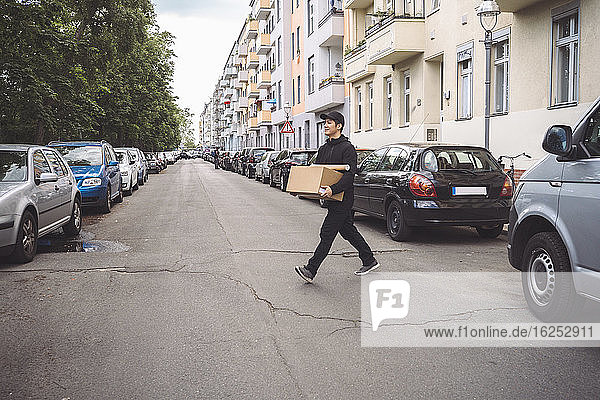 Zuversichtlicher Zusteller mit Pappkarton auf der Straße in der Stadt