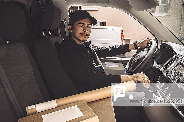 Portrait of confident delivery man with package driving truck