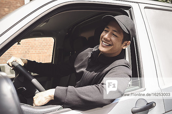 Lächelnder Lieferwagenfahrer schaut durchs Fenster  während er im Lastwagen sitzt