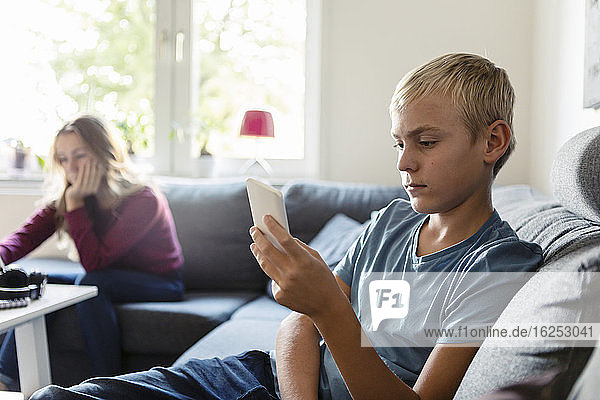 Männlicher Teenager telefoniert  während die Schwester zu Hause auf dem Sofa sitzt