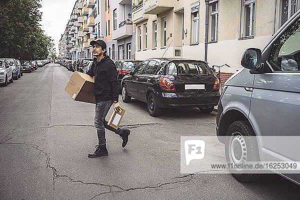 Zuversichtlicher Zusteller mit Paket  der in der Stadt auf der Straße geht