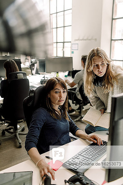 Weibliche Mitarbeiterin benutzt Computer  während der Unternehmer im Büro diskutiert