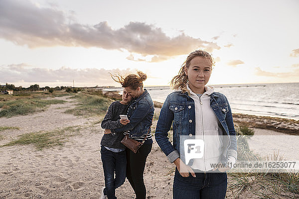 Portrait of teenager girl while mother embracing son at beach