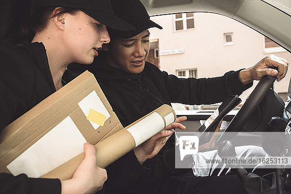 Männliche und weibliche Fahrer mit Paket schauen auf das digitale Tablett  während sie im Lkw sitzen