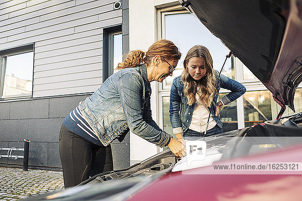 Alleinerziehende Mutter repariert Auto  während die Tochter am Straßenrand steht