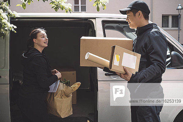 Zustellerin spricht mit lächelndem Kollegen  während sie ein Paket in der Nähe des Lastwagens hält