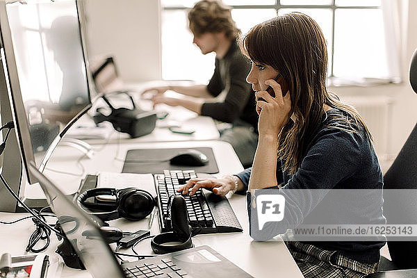 Unternehmerin  die am Computer arbeitet  während sie am Arbeitsplatz telefoniert