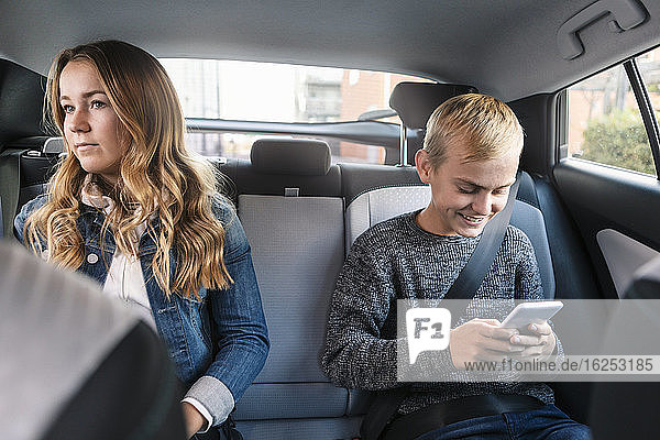 Smiling teenager using phone while sitting by sister in car