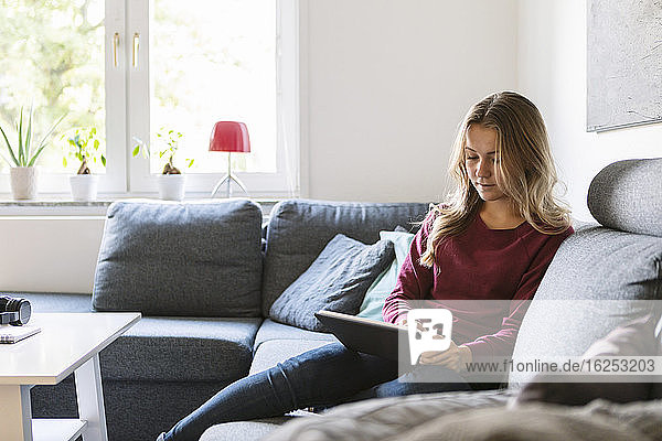 Weiblicher Teenager benutzt digitales Tablet  während er zu Hause auf dem Sofa sitzt