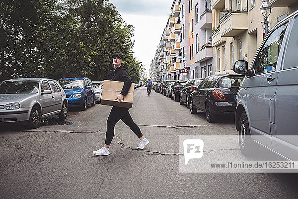 Side view of delivery woman with cardboard box walking on street in city