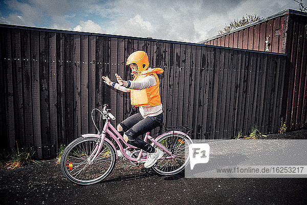 Lächelndes Mädchen fährt Fahrrad mit ausgestreckten Armen auf der Straße