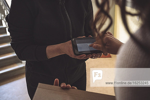 Midsection of customer signing on phone during home delivery