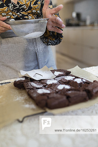 Frau bestreut gebackene Brownies in der Küche mit Puderzuckerherzen