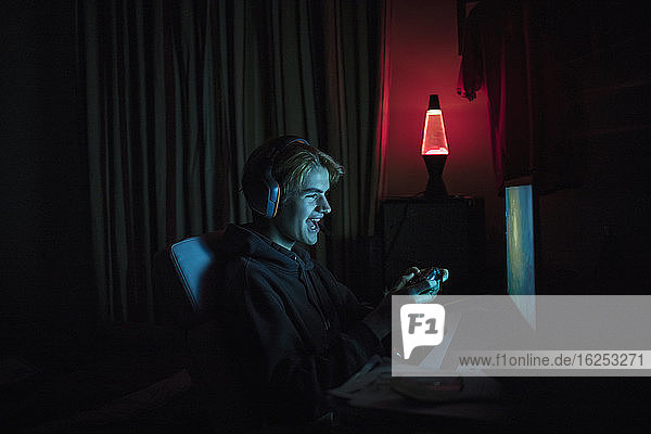 Lächelnder Teenager spielt Videospiel am Computer im dunklen Schlafzimmer