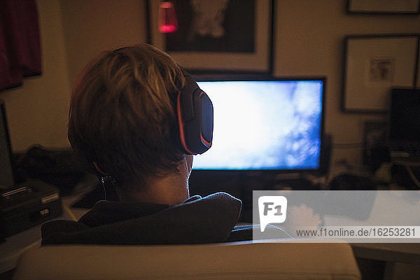 Teenager-Junge mit Kopfhörern spielt Videospiel im dunklen Schlafzimmer