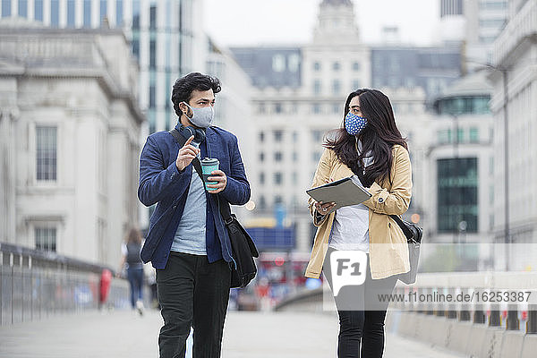 Geschäftsleute mit Gesichtsmasken im Gespräch auf einer städtischen Fußgängerbrücke