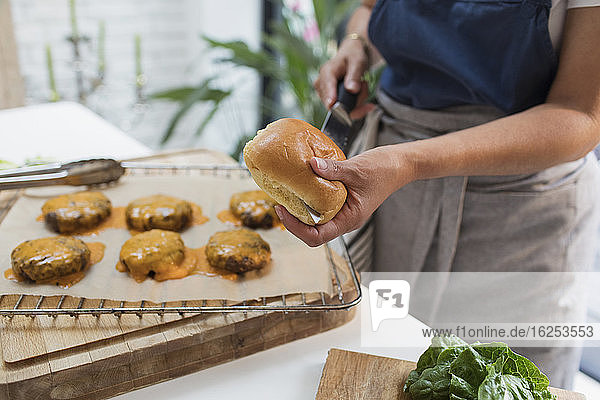 Frau kocht Cheeseburger und schneidet Hamburger-Brötchen in der Küche