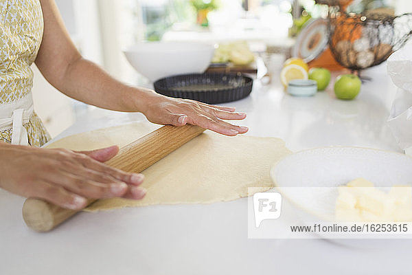 Frau rollt Kuchenteig mit Nudelholz auf der Küchentheke aus
