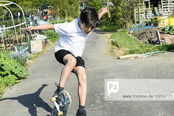 Junge mit braunem Haar  der ein T-Shirt und Shorts trägt und einen Skateboardtrick vorführt.