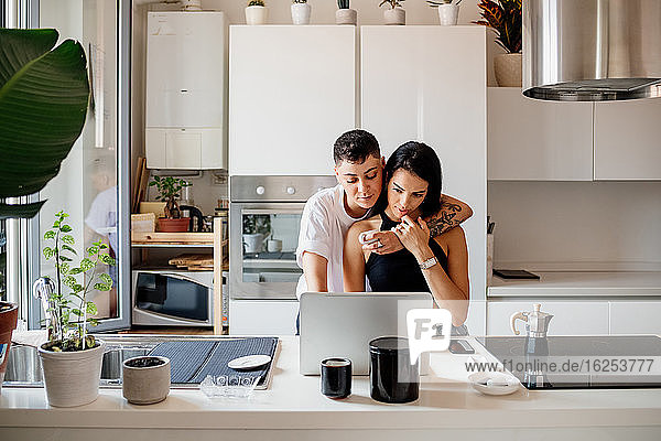 Young lesbian couple standing in kitchen  using laptop.