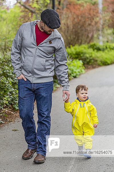 Father holding hands with young daughter while taking a walk in the park; North Vancouver  British Columbia  Canada