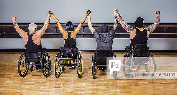 Ein Blick von hinten auf eine Gruppe querschnittsgelähmter Freunde  die nach einem Training in einer Fitnesseinrichtung bei einer Siegesfeier die Hände hoch halten: Sherwood Park  Alberta  Kanada
