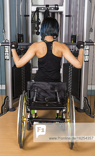 A view from behind of a paraplegic woman working out using a lat pull down machine in a fitness facility; Sherwood Park  Alberta  Canada