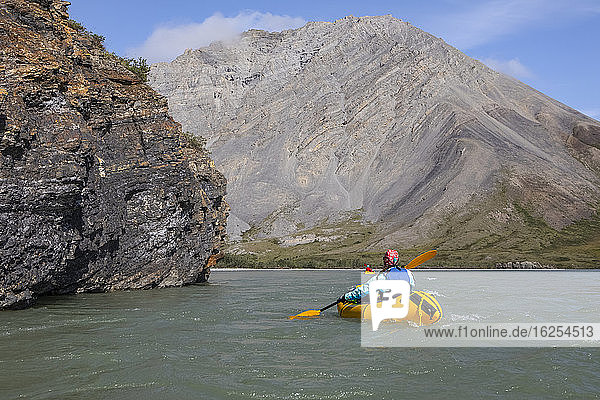 Two women paddling past rock feature on the Canning River in yellow packraft boats  Brooks Range  Arctic National Wildlife Refuge; Alaska  United States of America
