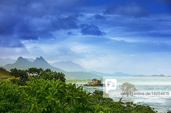Nebel über der Kaupo-Bucht bei Sonnenaufgang mit einem Pier der zu einem Haus führt und Bergspitzen die die Küste säumen; Oahu Hawaii Vereinigte Staaten von Amerika