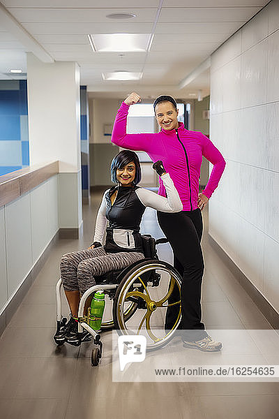 A paraplegic woman and her trainer show off their muscles while posing for the camera in a hallway in a recreational facility: Sherwood Park  Alberta  Canada