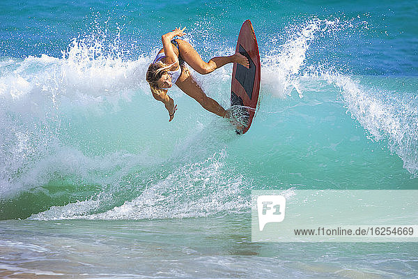 Eine junge Frau reitet auf einem Skimboard auf einer Welle vor Sandy Beach  Oahu; Oahu  Hawaii  Vereinigte Staaten von Amerika