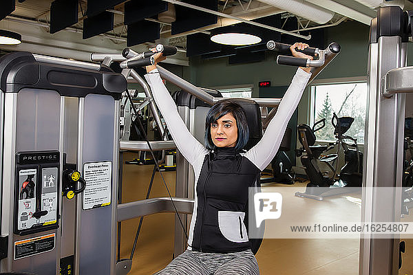 Eine querschnittsgelähmte Frau trainiert mit einer Überkopfpresse in einer Fitnesseinrichtung; Sherwood Park  Alberta  Kanada