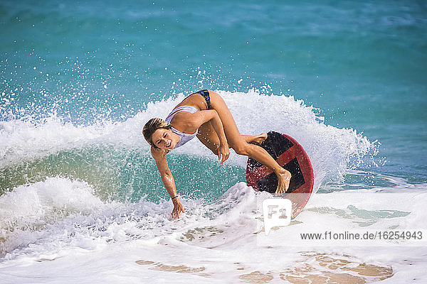 Eine junge Frau  die auf einer Welle vor Sandy Beach  Oahu; Oahu  Hawaii  Vereinigte Staaten von Amerika  auf dem Skimboard fährt
