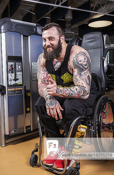 A paraplegic man looking at the camera and giving an affirming hand gesture after working out using an overhead press in a fitness facility; Sherwood Park  Alberta  Canada